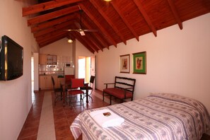A room with a bed, a desk, and a chair. There is a kitchenette in the background. - Cabañas Marina House (Termas de Rio Hondo)