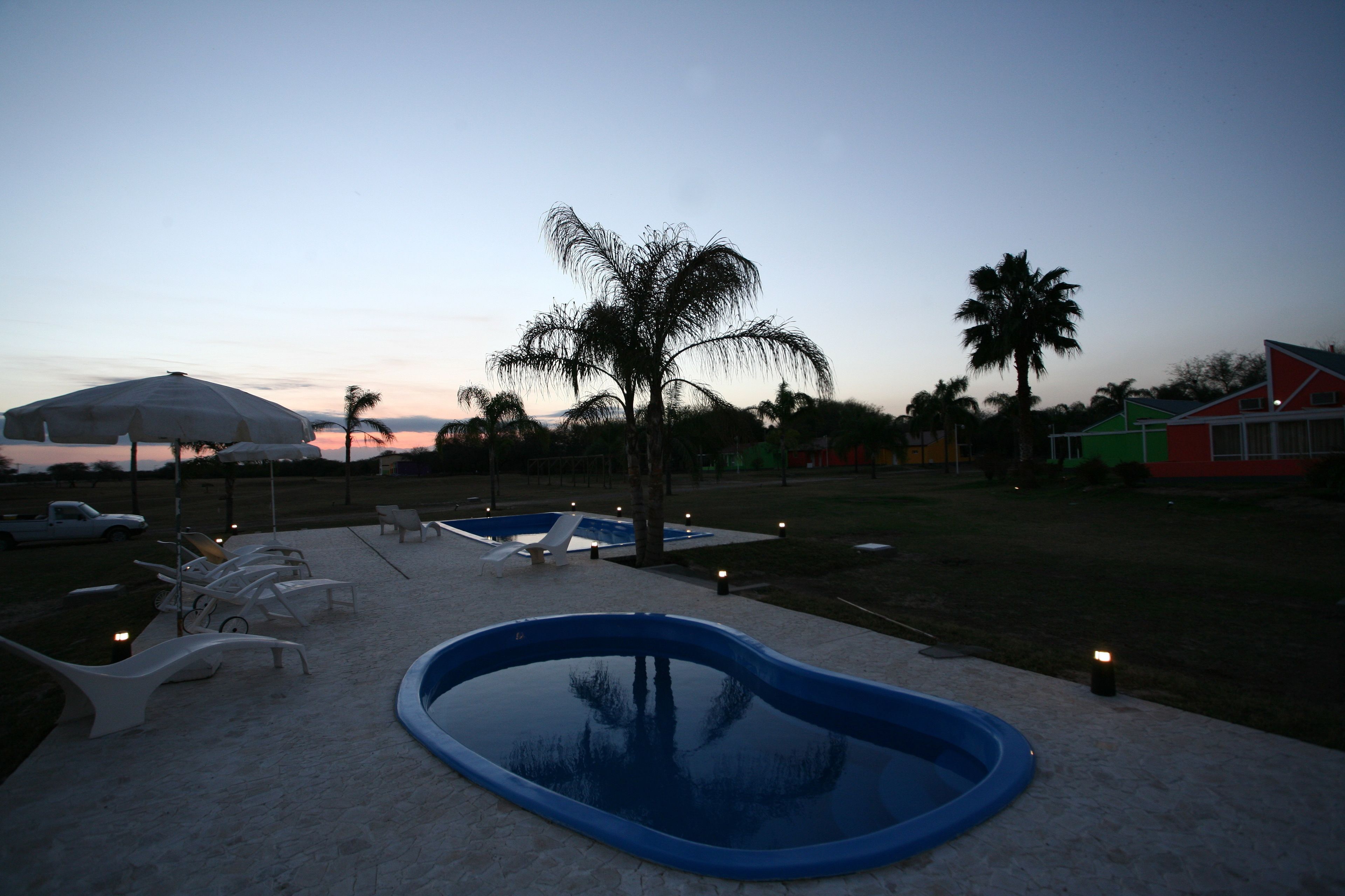 A pool area with lounge chairs and a small pool, surrounded by palm trees and a sunset in the background.