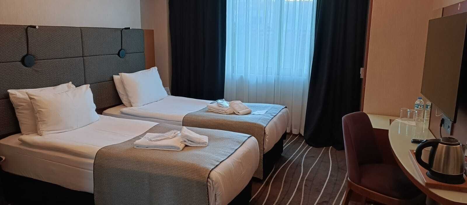Une chambre d’hôtel avec deux lits, un bureau avec une bouilloire et une chaise.