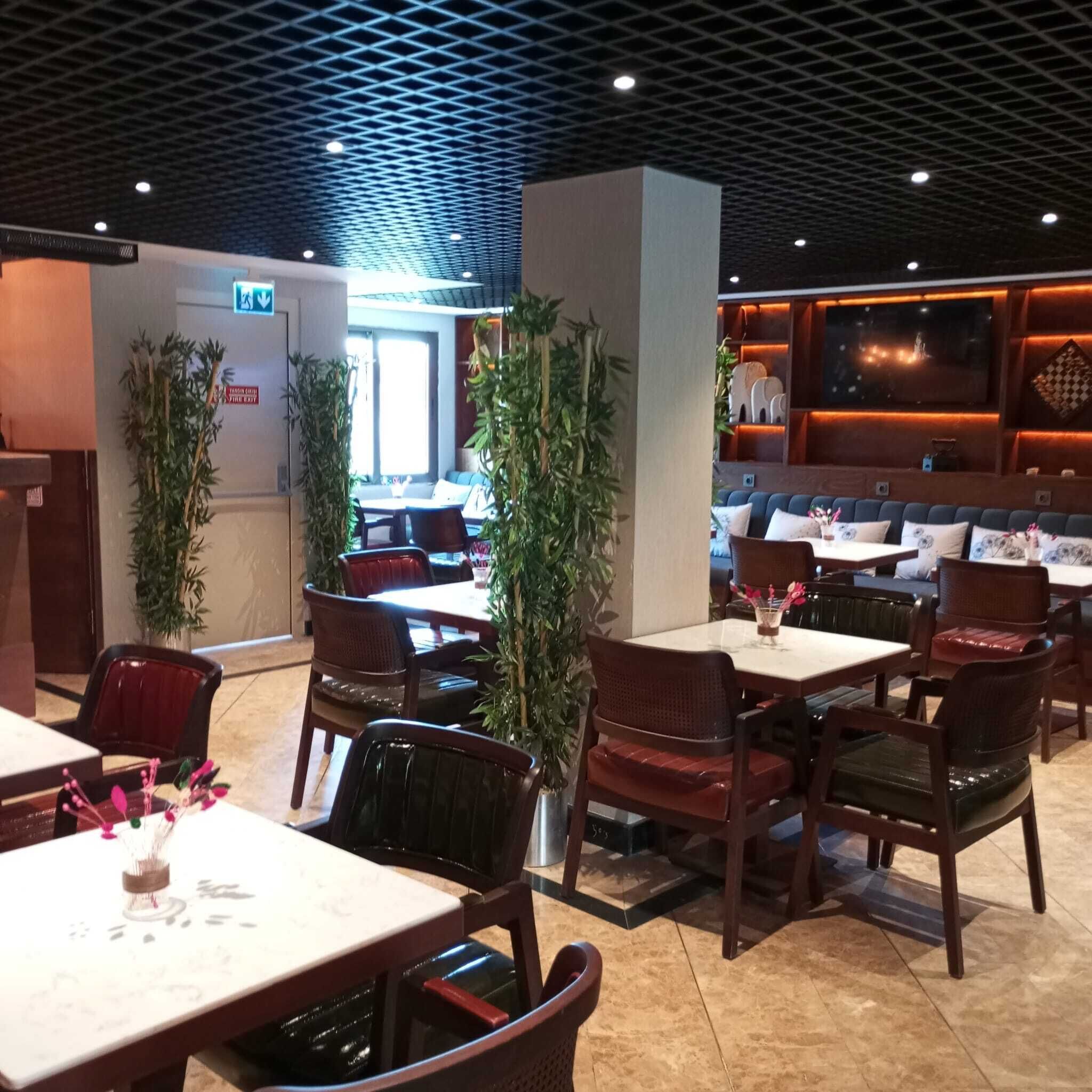 A restaurant interior with multiple dining tables and chairs, a patterned ceiling, and a view of the outside.