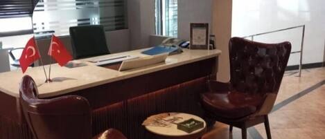 A modern reception area with a counter, two leather chairs, and a small table with a menu.