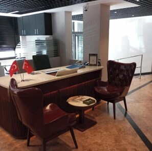 A modern reception area with a counter, two leather chairs, and a small table with a menu.