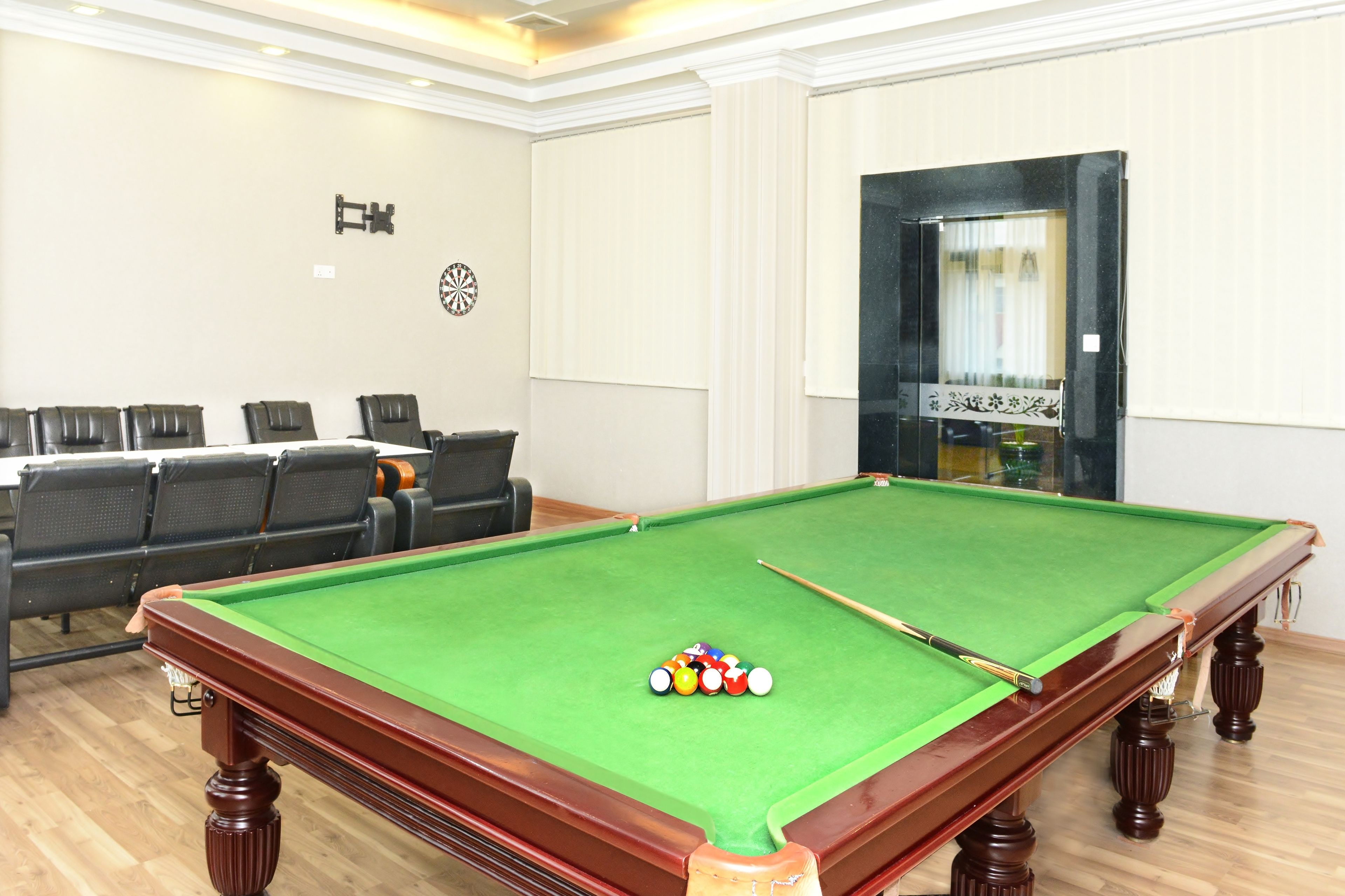 A pool table with balls, a sofa, and chairs in a room with a wooden floor and white walls.