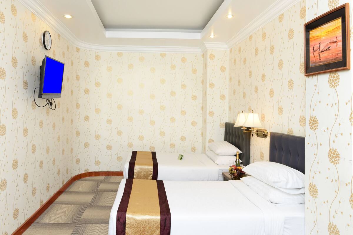A hotel room with two beds, a TV, a clock, and a framed picture on the wall.