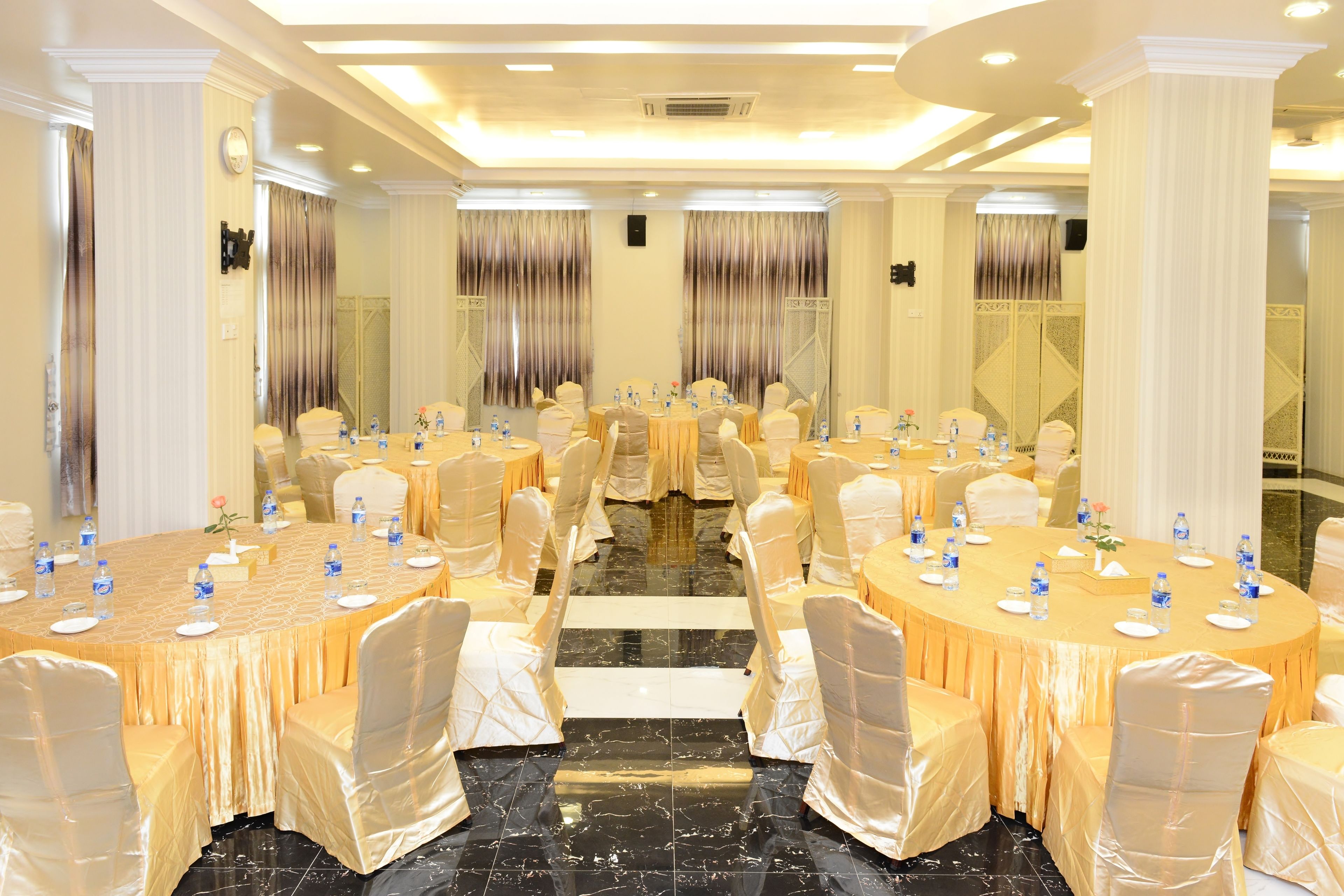 A banquet hall with round tables, chairs, and a central aisle. Tables are set with water bottles and plates.