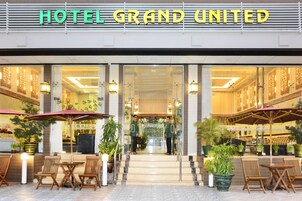 La entrada del Hotel Grand United con asientos exteriores e instalación de plantas en macetas.