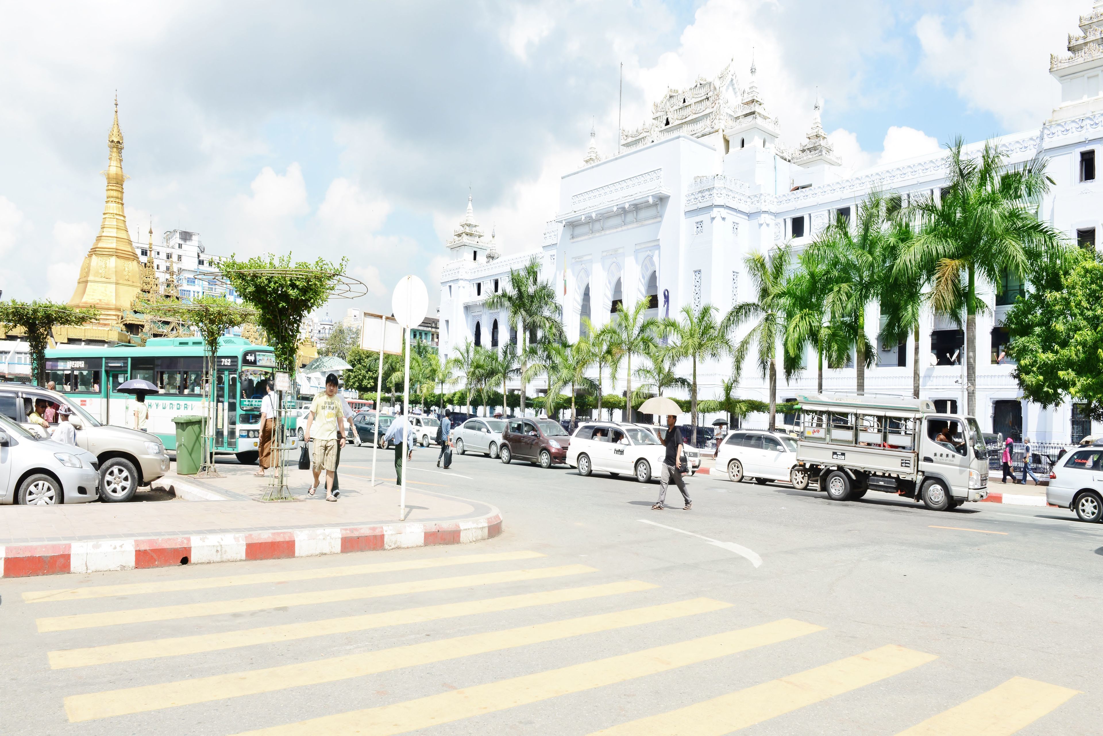 A street with a large white building, a golden pagoda, and palm trees.
