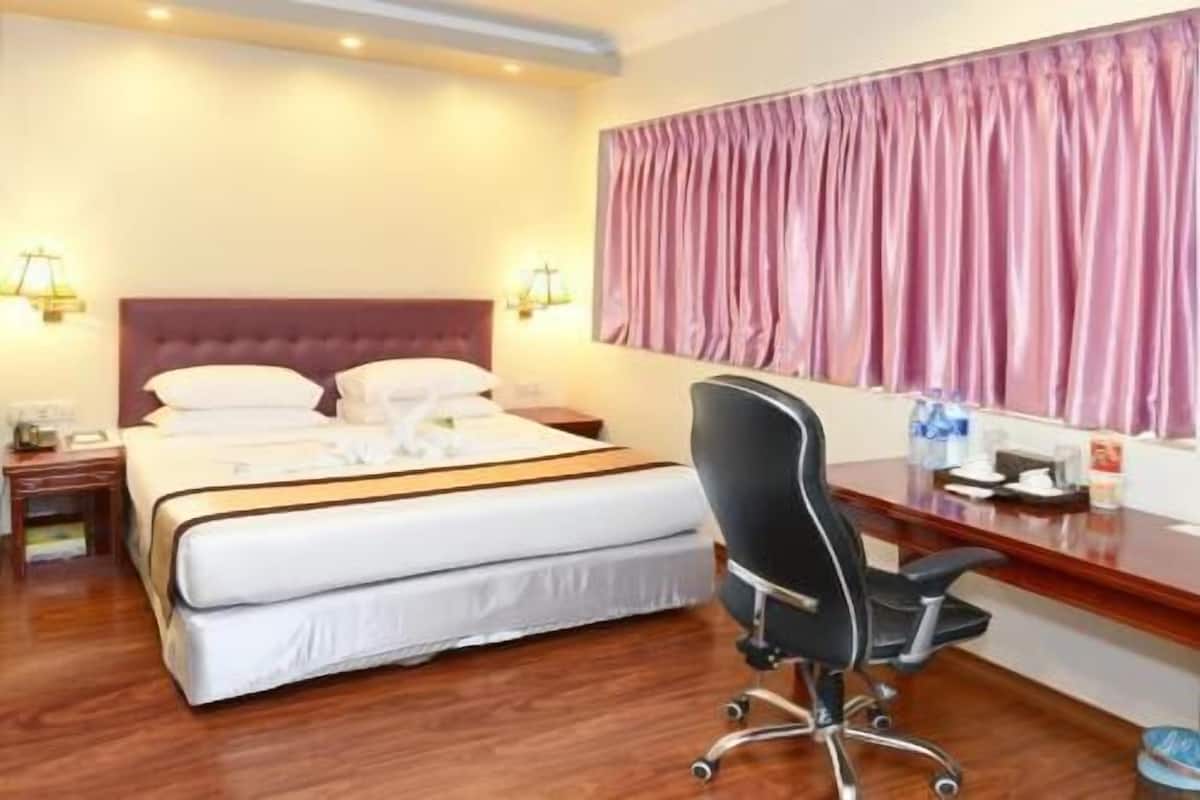A hotel room with a bed, a desk, a chair, a nightstand, and a window with curtains.