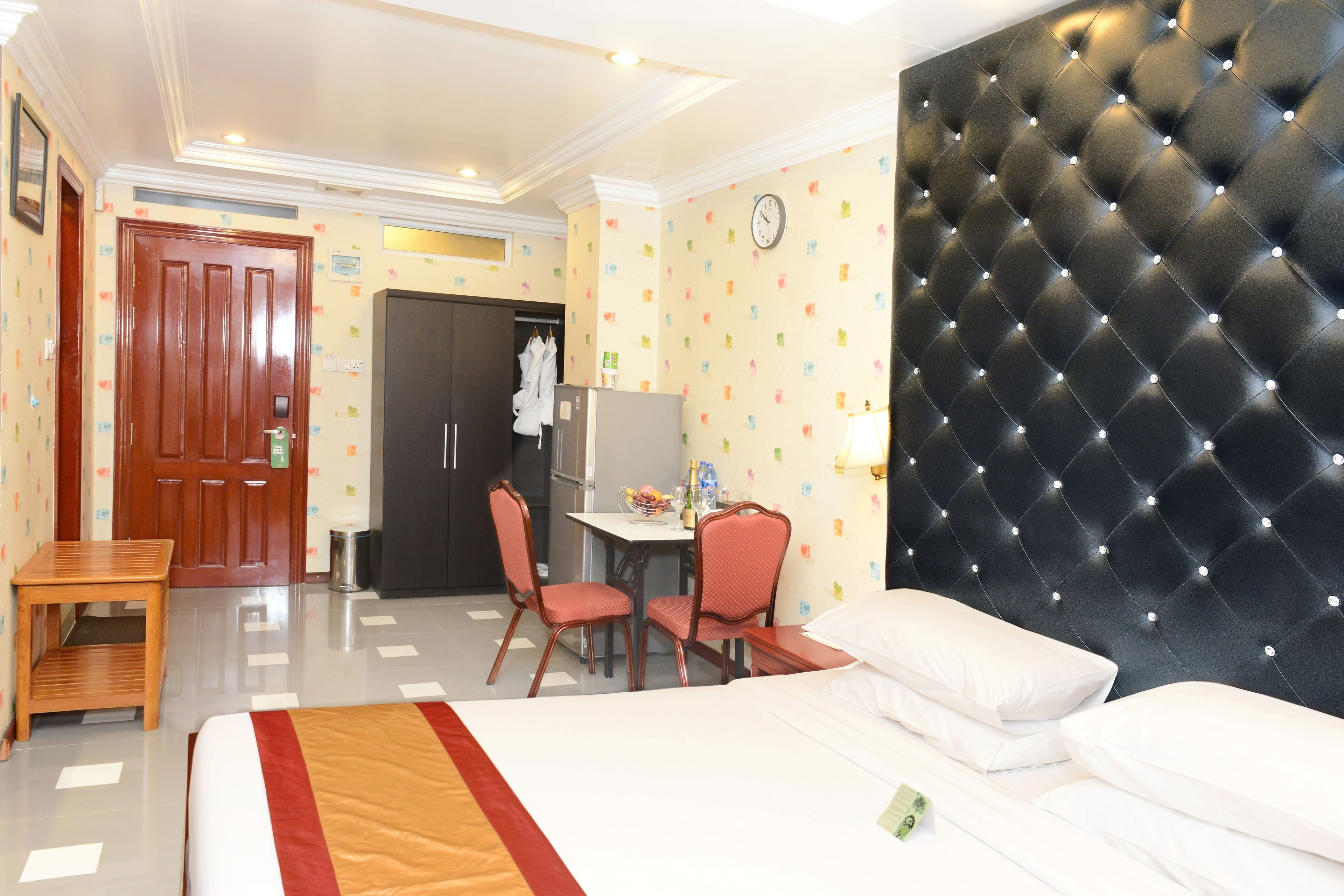 A hotel room with a bed, a desk with chairs, a wardrobe, and a wall clock.