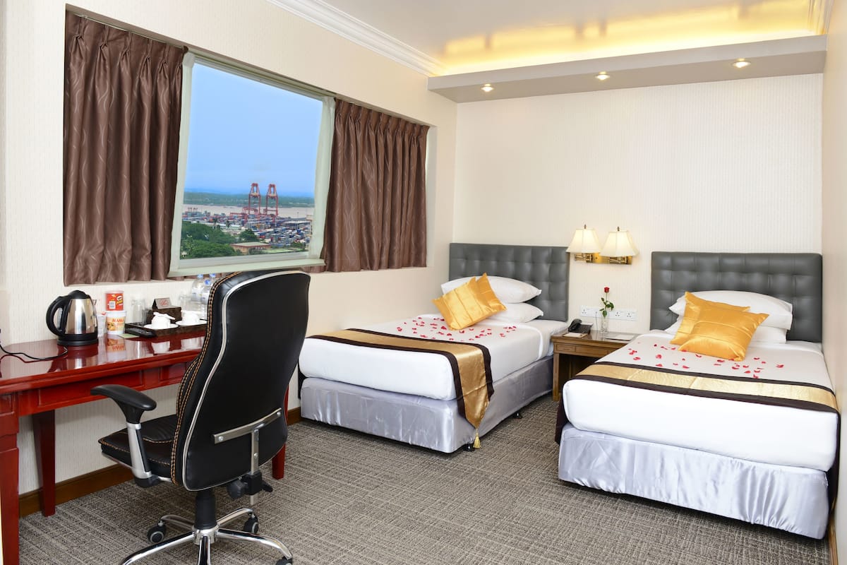 A hotel room with two beds, a desk, and a chair. There is a window with curtains, a view of a bridge, and a lamp on the nightstand.