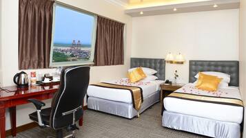 A hotel room with two beds, a desk, and a chair. There is a window with curtains, a view of a bridge, and a lamp on the nightstand.
