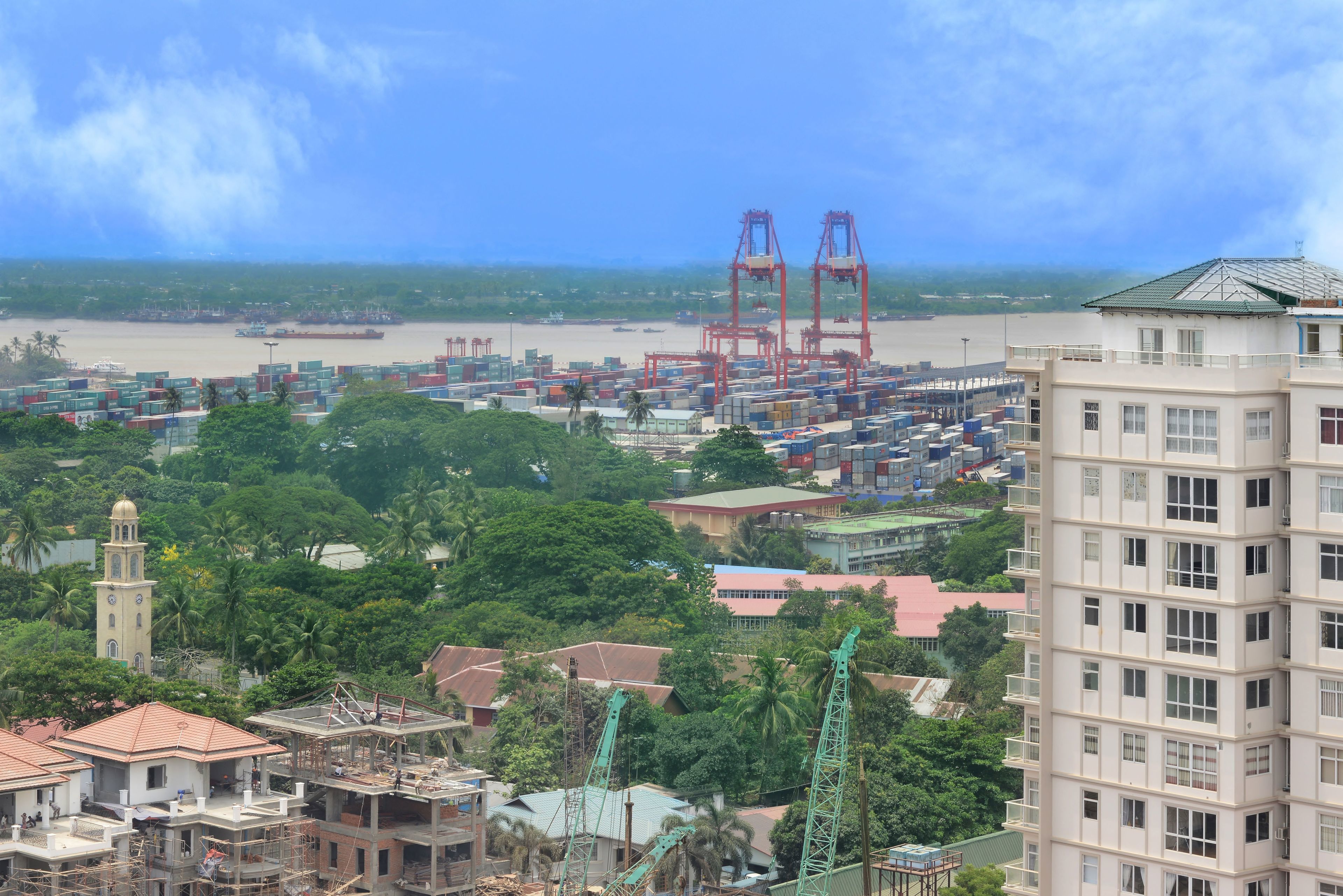 A coastal cityscape with a port, cranes, and residential buildings.