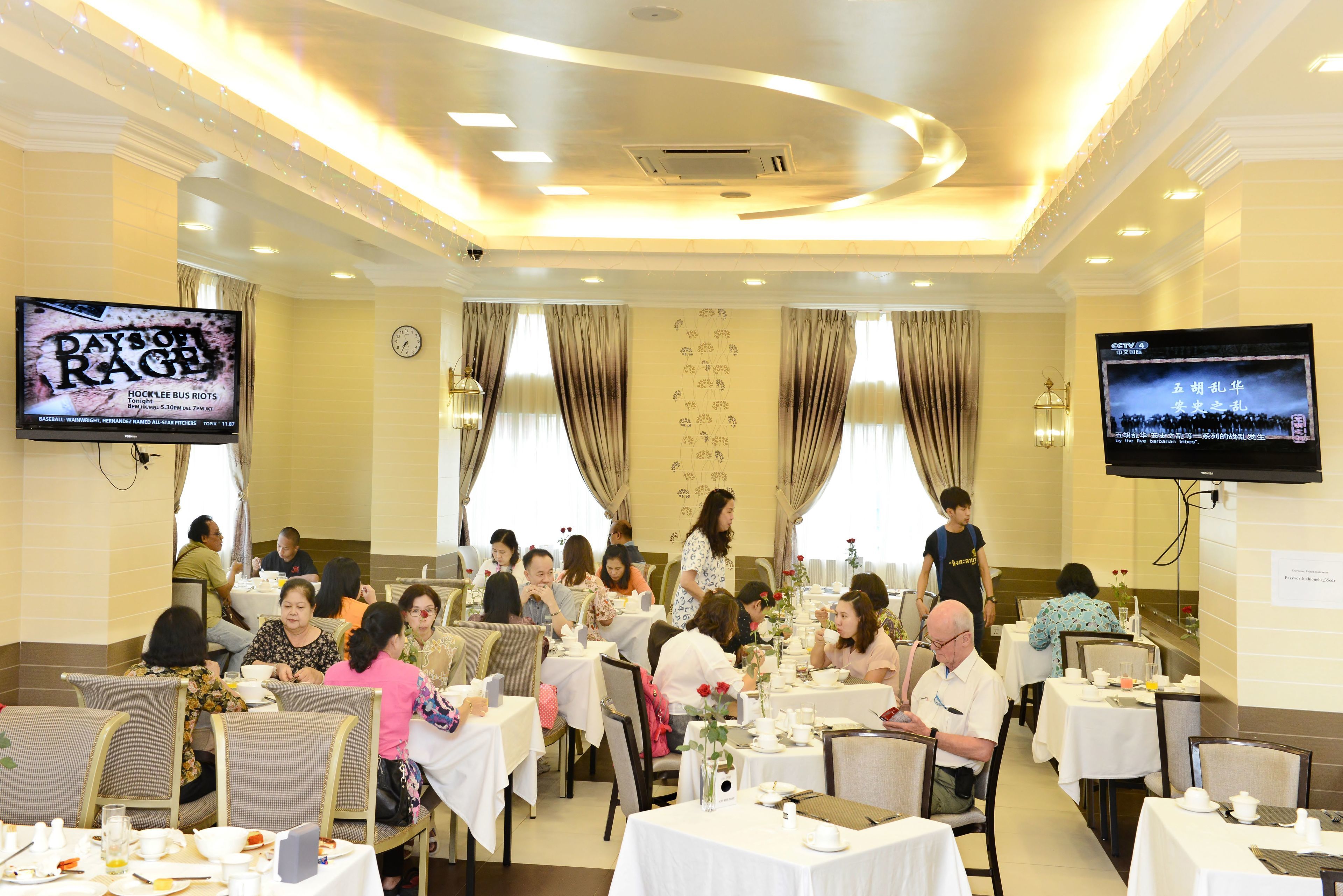 A dining area with multiple tables and chairs, a clock on the wall, and two televisions mounted on the walls.