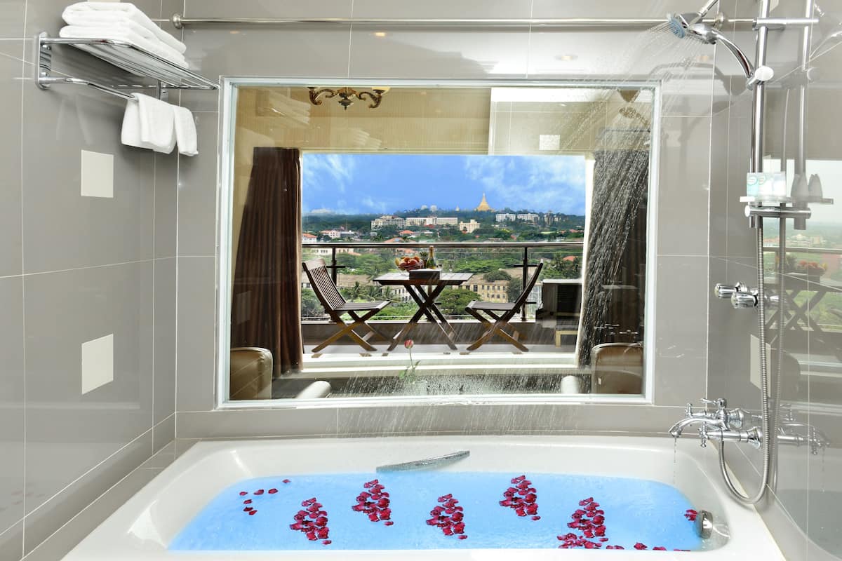 A bathroom with a bathtub, shower, and a view of a balcony with a table and chairs.