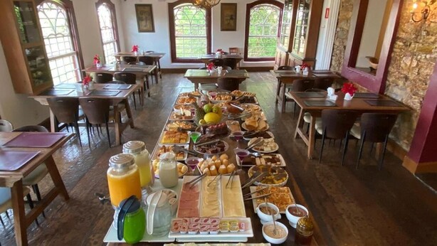 A buffet setup with various food items and drinks in a room with wooden floors and large windows. - Hotel Solar das Lajes (Ouro Preto)