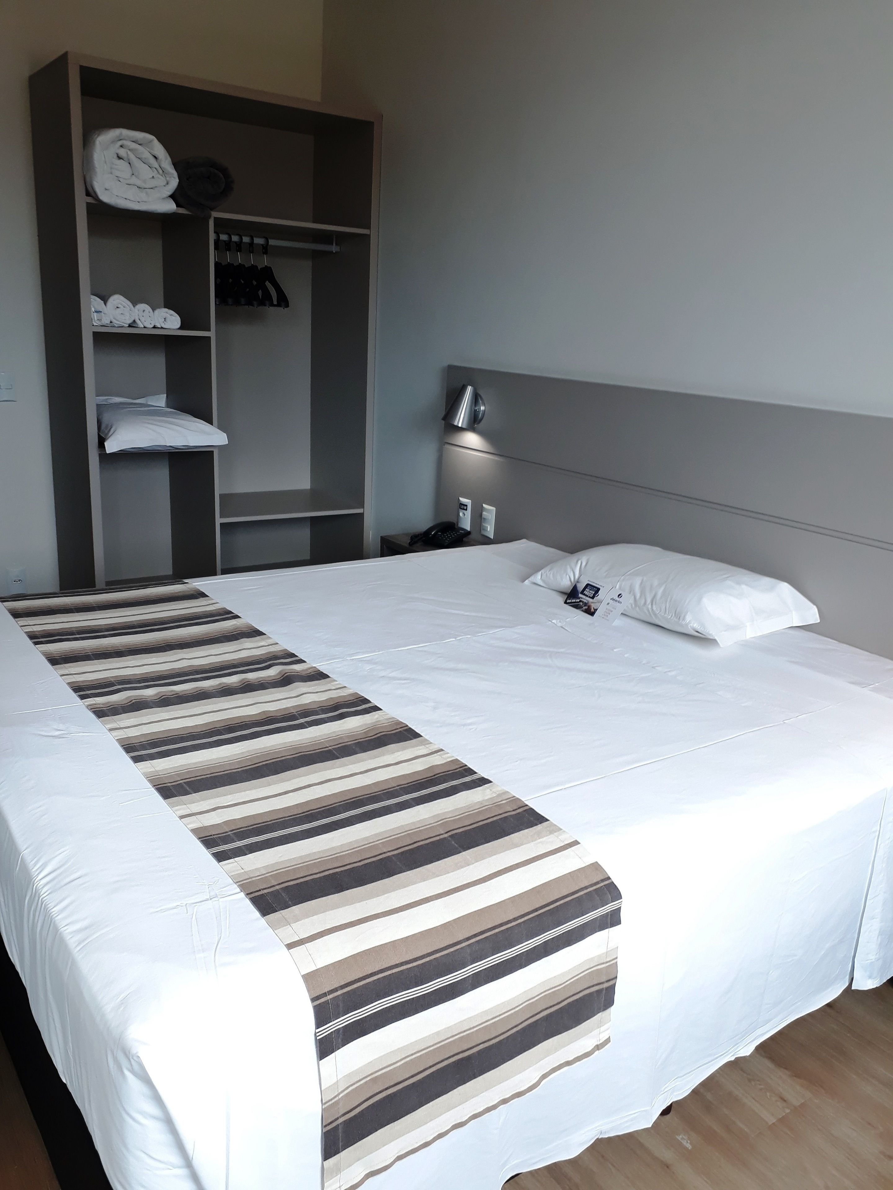 Een hotelkamer met een groot bed, een kledingkast, een nachtkastje met een lamp en een telefoon.