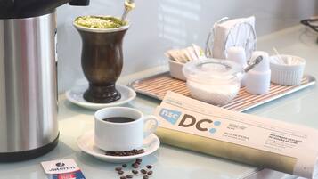 A coffee station with a coffee maker, cup, and saucer, a small bowl of coffee beans, and a card with text.
