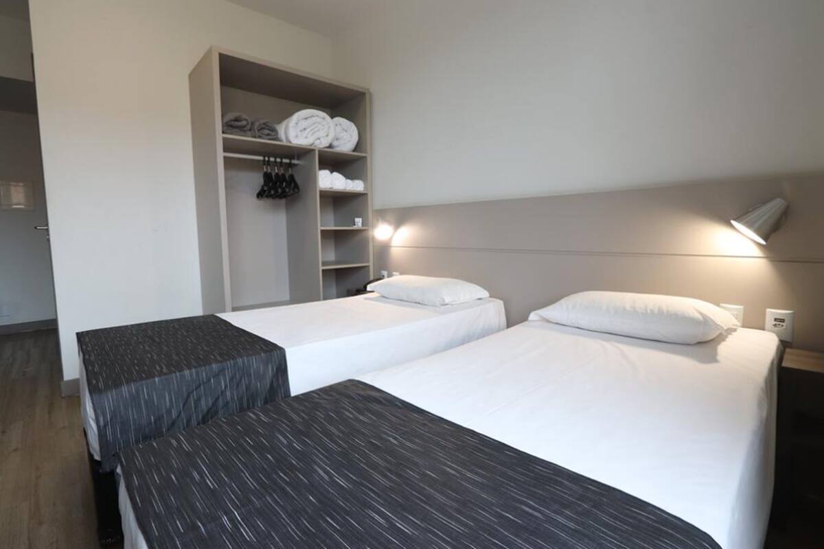 A hotel room with two beds, a wardrobe, and a desk.