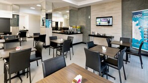 A modern hotel dining area with multiple tables and chairs, a kitchen in the background, and a large poster on the wall. - Hotel Valerim Itajaí (Itajai)