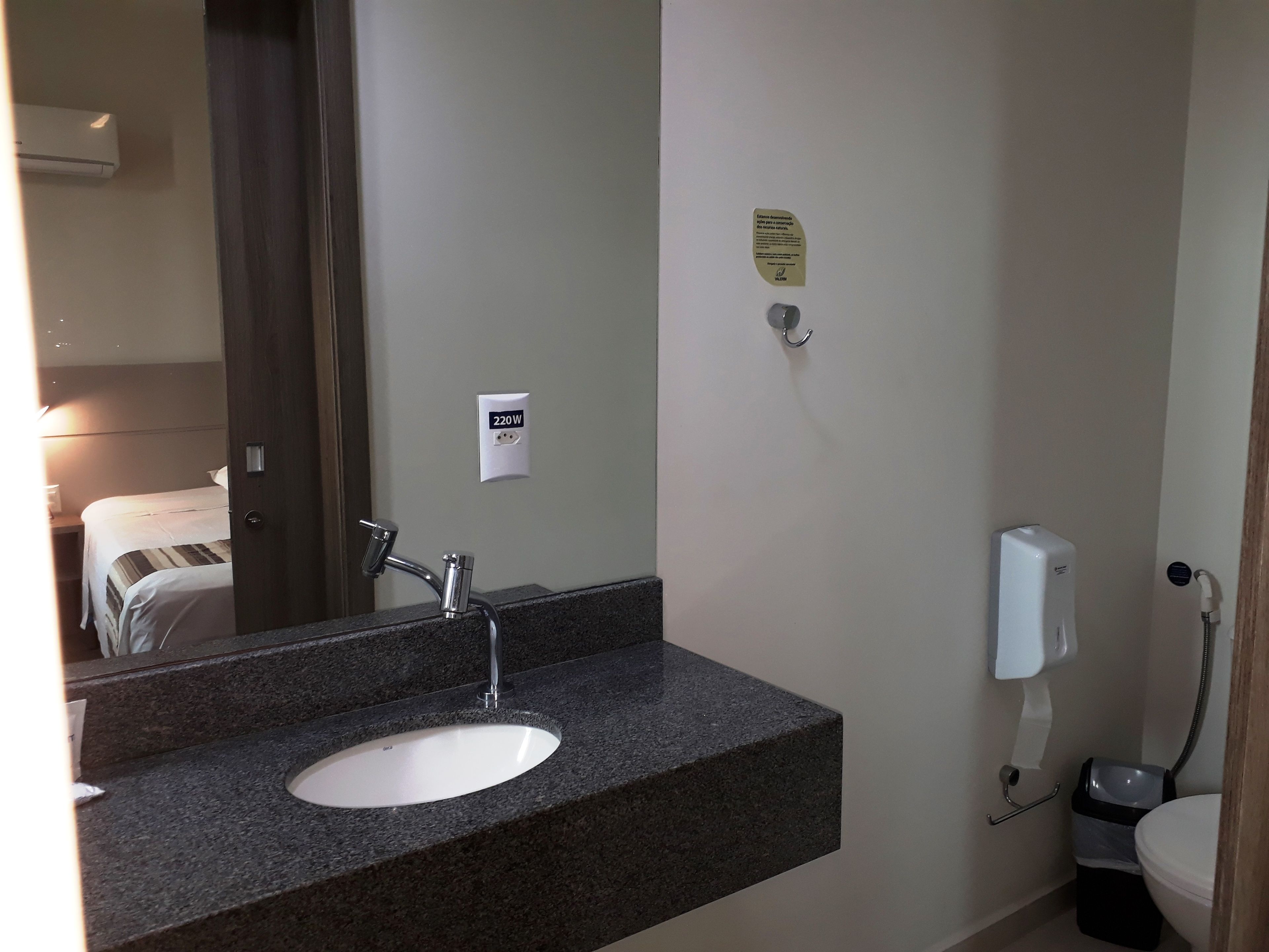 A bathroom with a granite countertop sink, a mirror, a towel rack, a toilet, and a hand dryer.