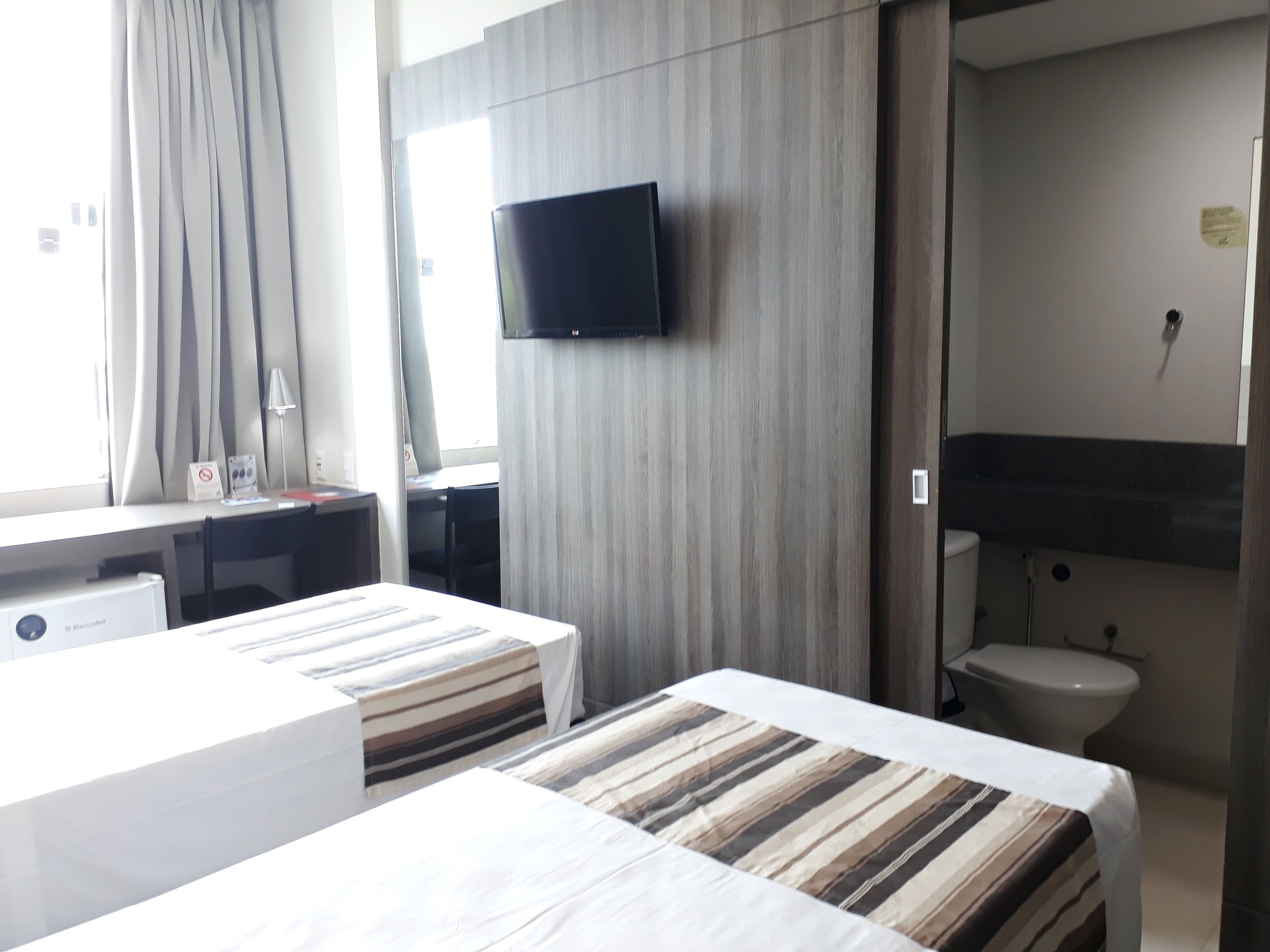 A hotel room with a bed, a desk, a TV mounted on the wall, and a toilet.