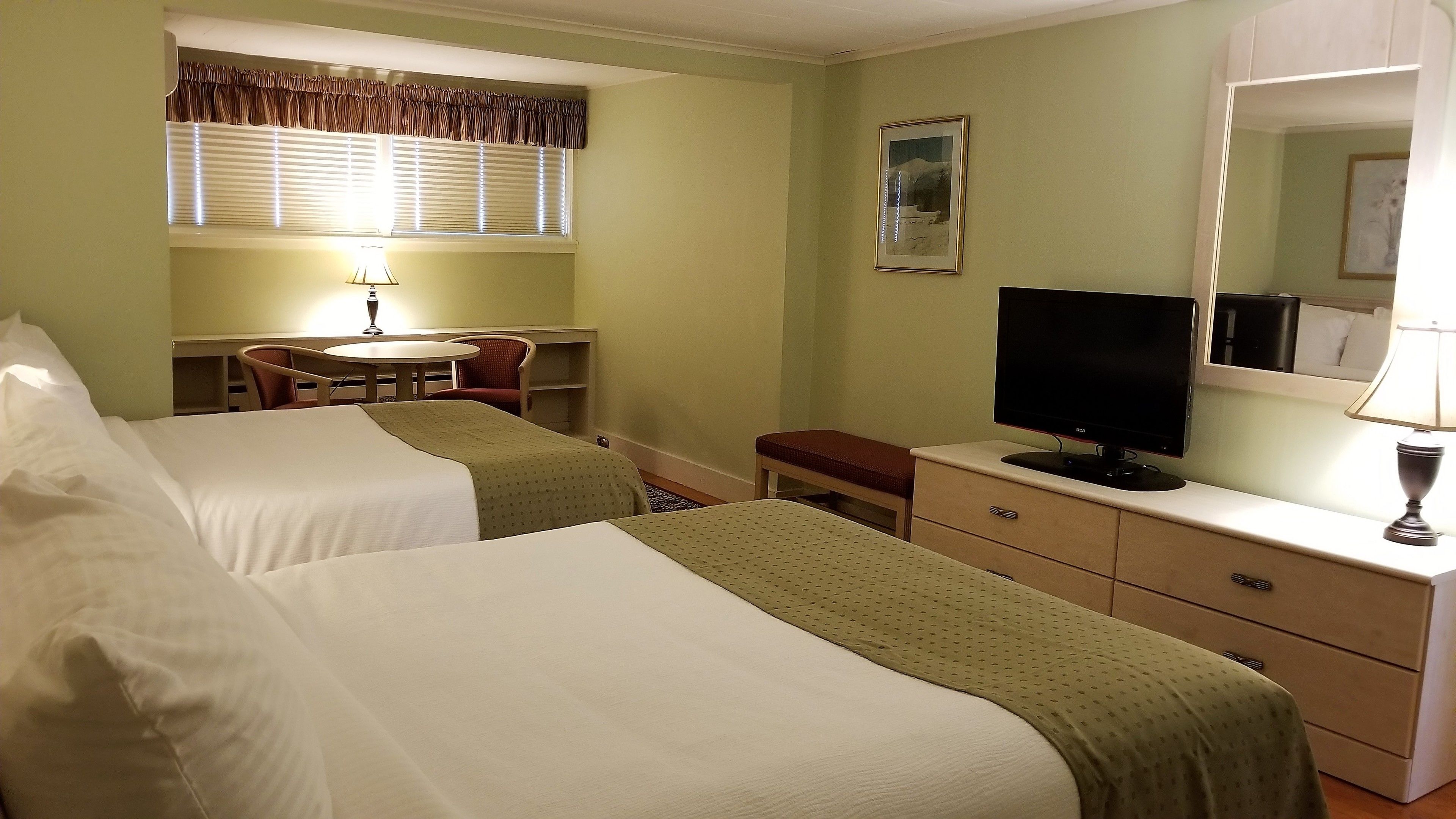 Una habitación de hotel con dos camas, un escritorio con silla, televisión y ventana con cortinas.