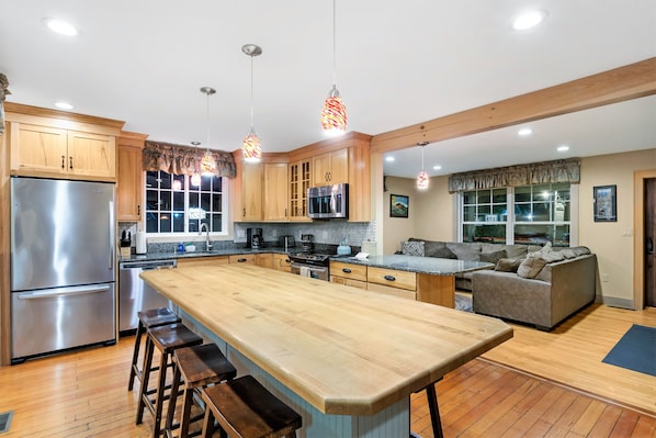 A spacious kitchen with wooden cabinets, stainless steel appliances, and a large island with stools. - Top Notch Inn (Gorham)