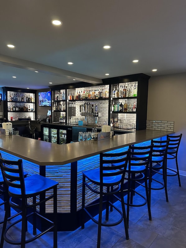 A bar area with a long counter, multiple shelves of bottles, glasses, and a television screen. - Top Notch Inn (Gorham)