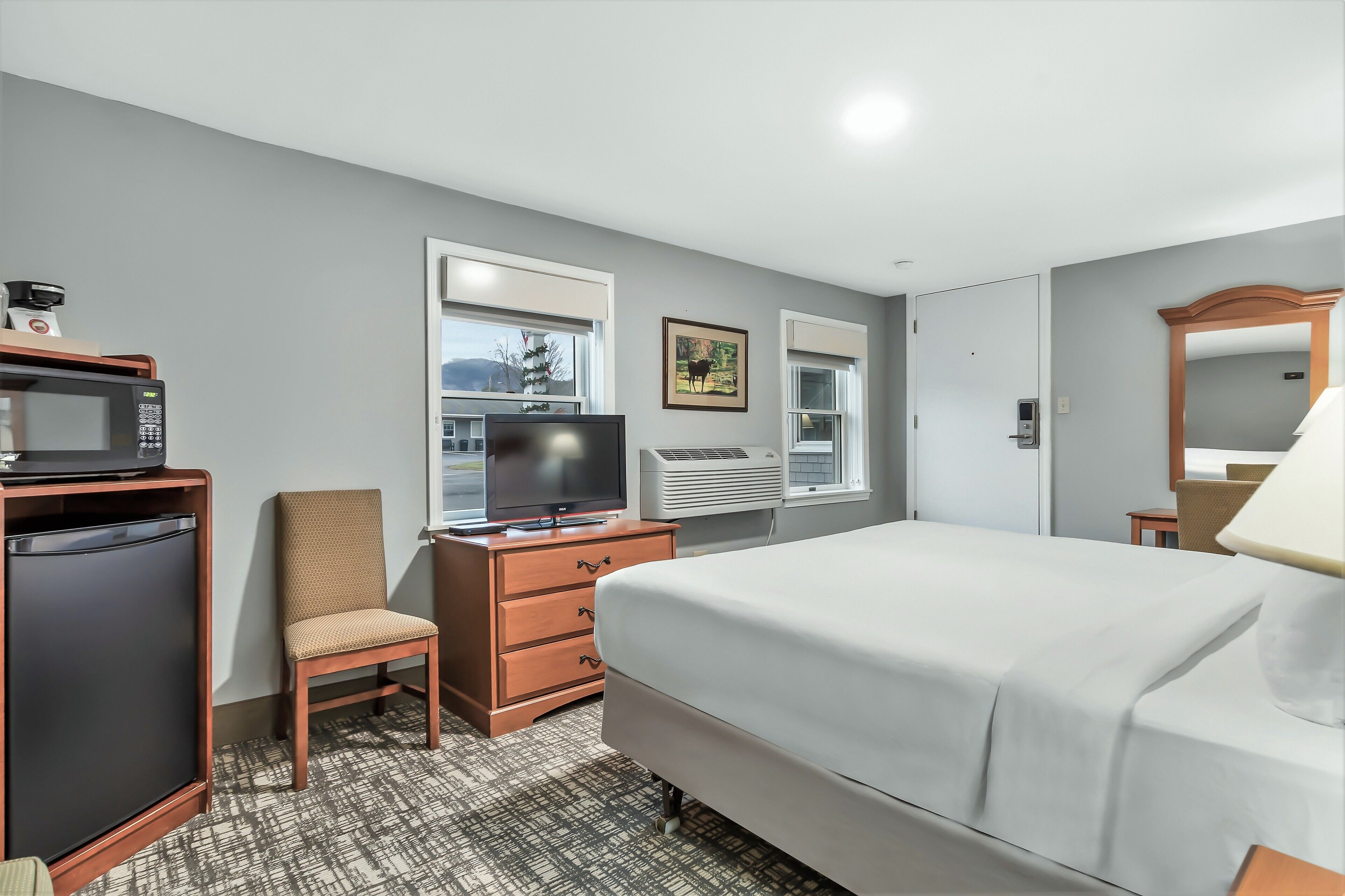 Une chambre d’hôtel équipée d’un lit, d’une télévision, d’une commode, d’une chaise et d’un four à micro-ondes.