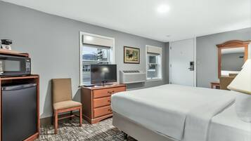 Une chambre d’hôtel équipée d’un lit, d’une télévision, d’une commode, d’une chaise et d’un four à micro-ondes.