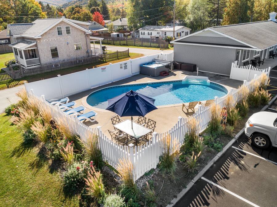 A swimming pool with lounge chairs and umbrellas, surrounded by a white picket fence and various plants.