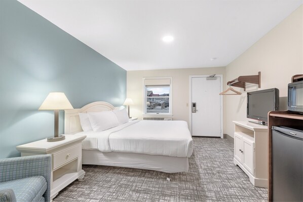 A hotel room with a bed, bedside tables, a TV, a wardrobe, and a view of the outside. - Top Notch Inn (Gorham)