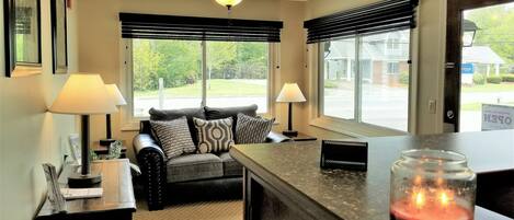A cozy living room with a sofa, two lamps, a ceiling fan, and a view of the outside.