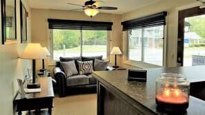 A cozy living room with a sofa, two lamps, a ceiling fan, and a view of the outside.