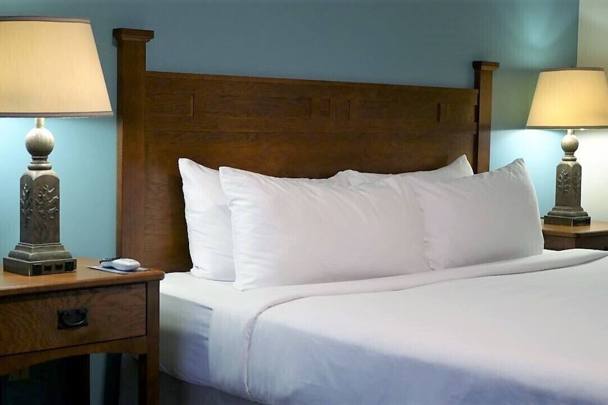 Una cama bien tendida con sábanas blancas, dos lámparas de noche y un cabecero de madera.
