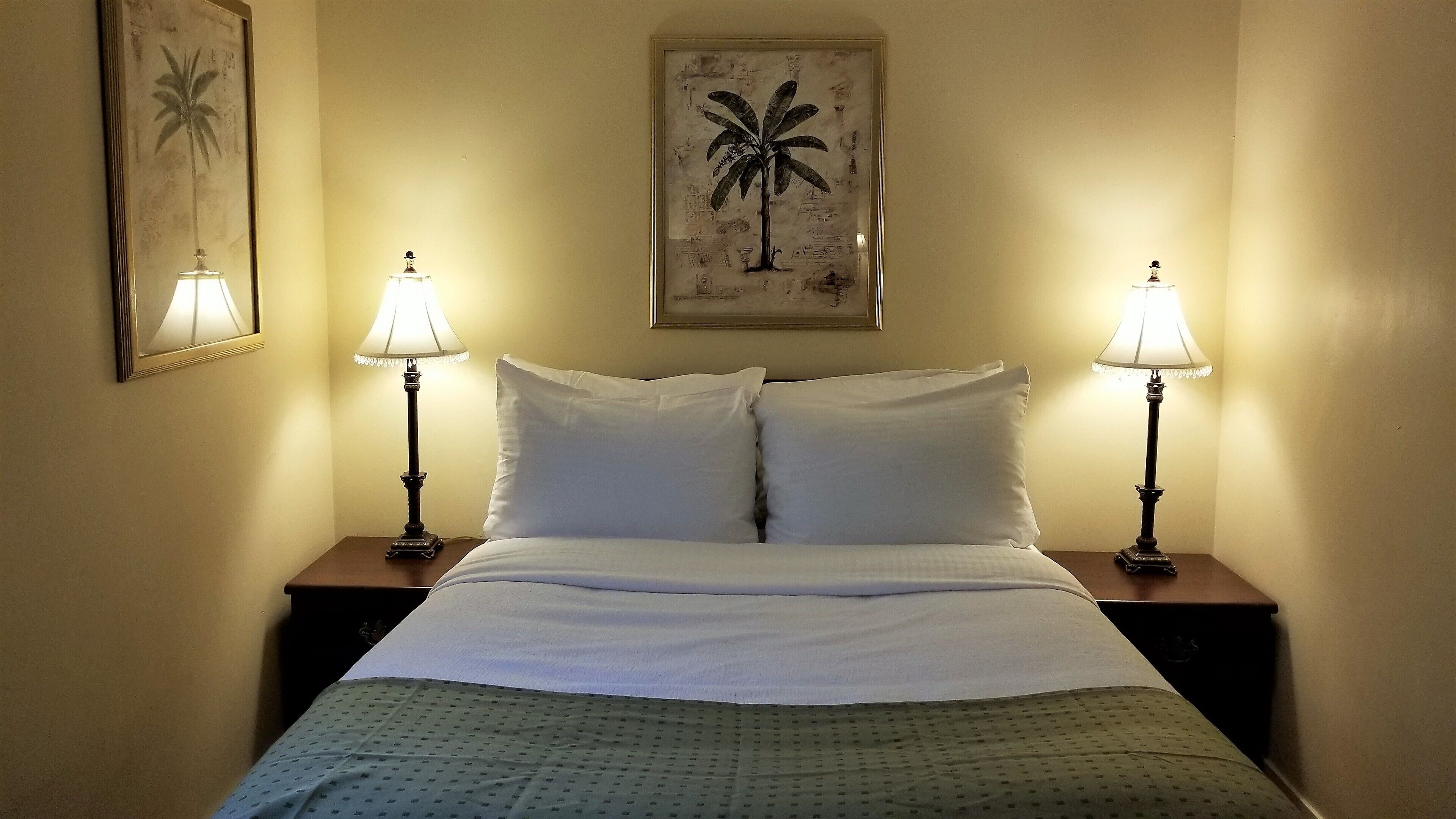 Une chambre d’hôtel avec un lit, deux tables de chevet, deux lampes et deux tableaux encadrés accrochés aux murs.