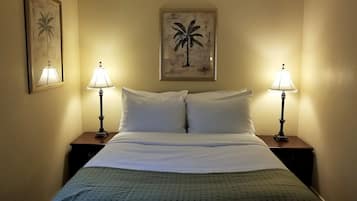 Une chambre d’hôtel avec un lit, deux tables de chevet, deux lampes et deux tableaux encadrés accrochés aux murs.