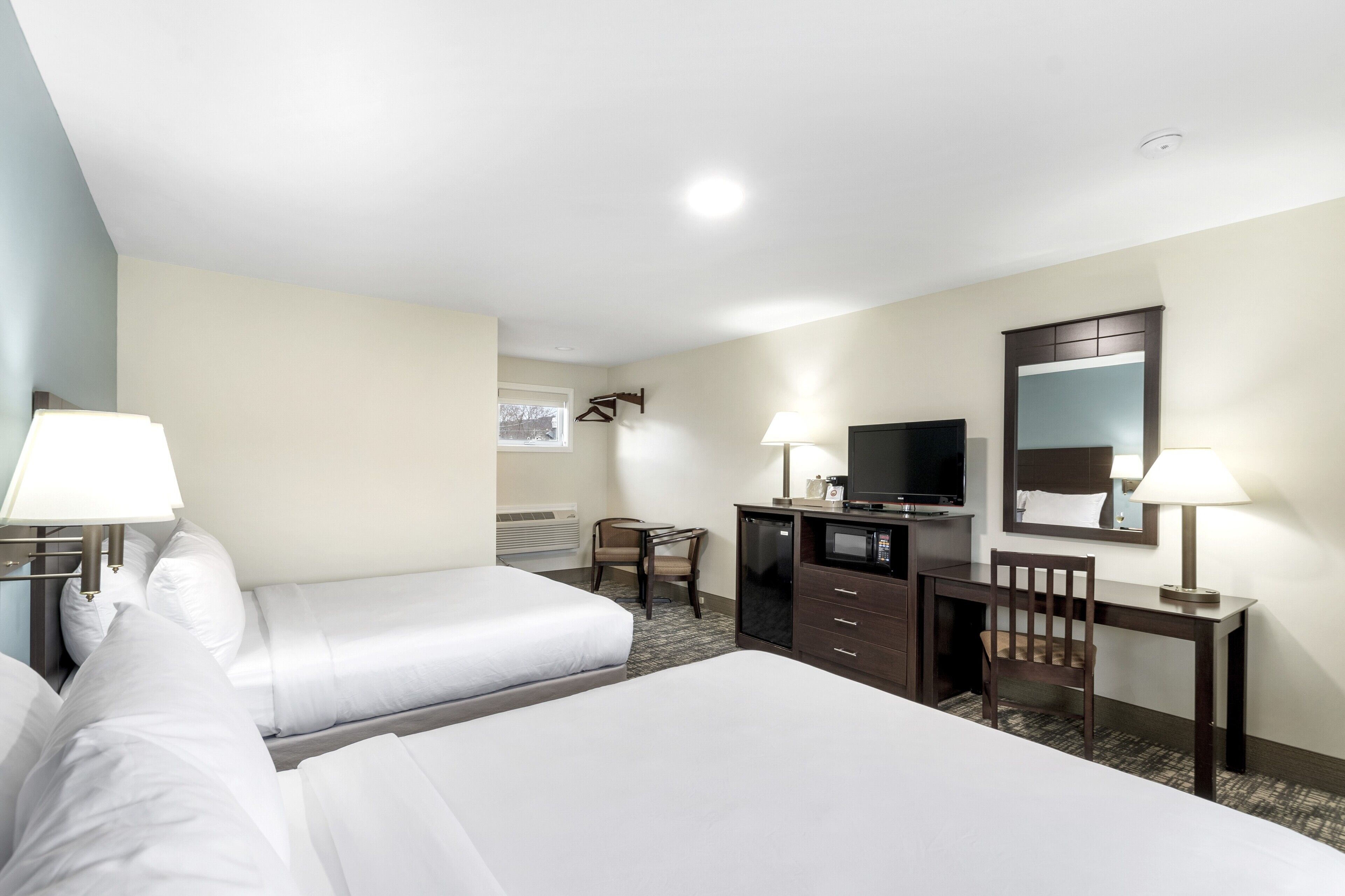 A hotel room with two beds, a desk, a television, and a mirror.