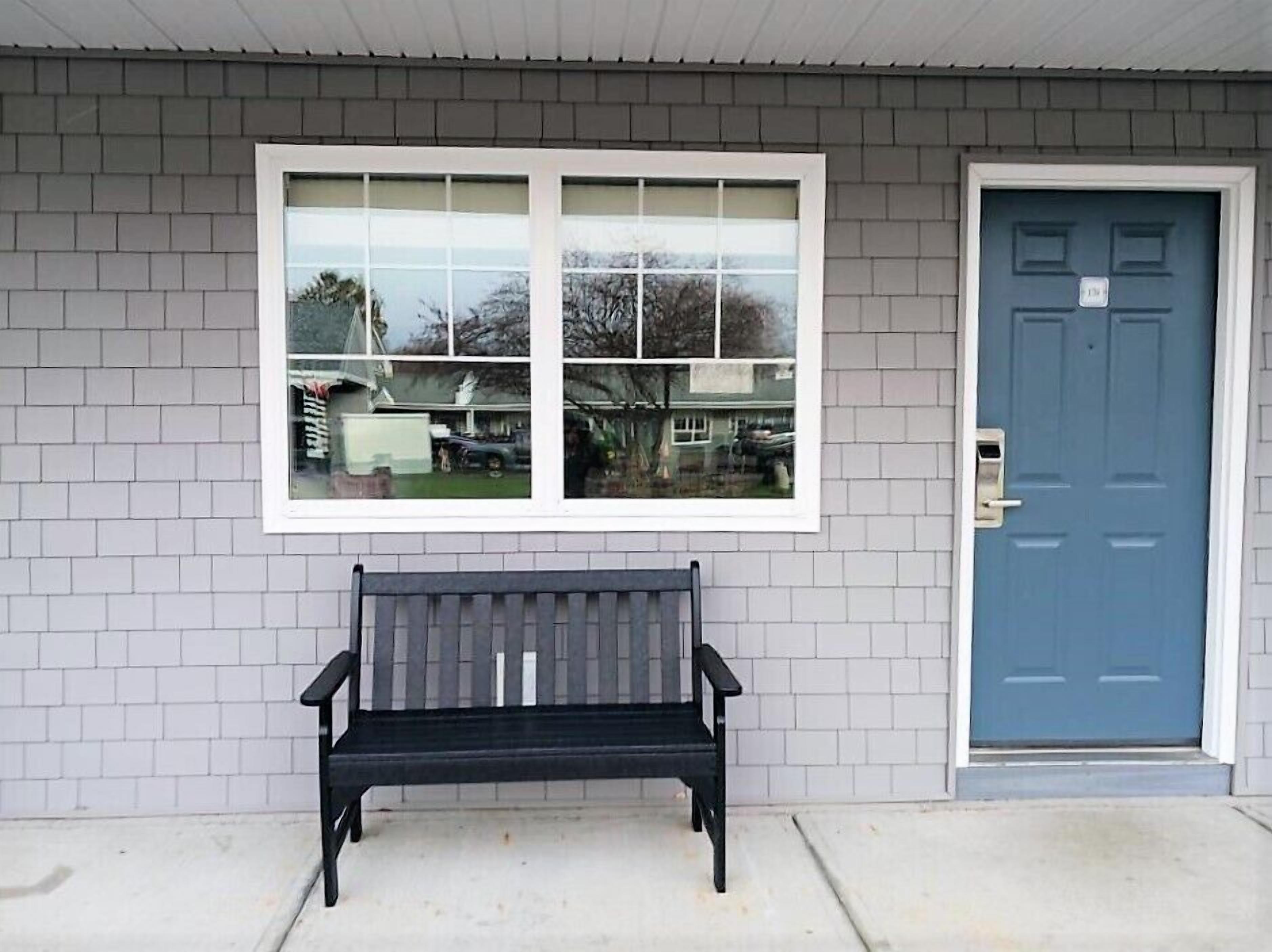 A building with a blue door, a bench in front, and a window reflecting a garage and trees.