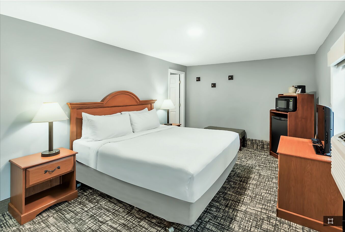Habitación de hotel con cama, mesita de noche con lámpara, televisión y minibar.