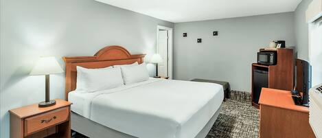 Habitación de hotel con cama, mesita de noche con lámpara, televisión y minibar.