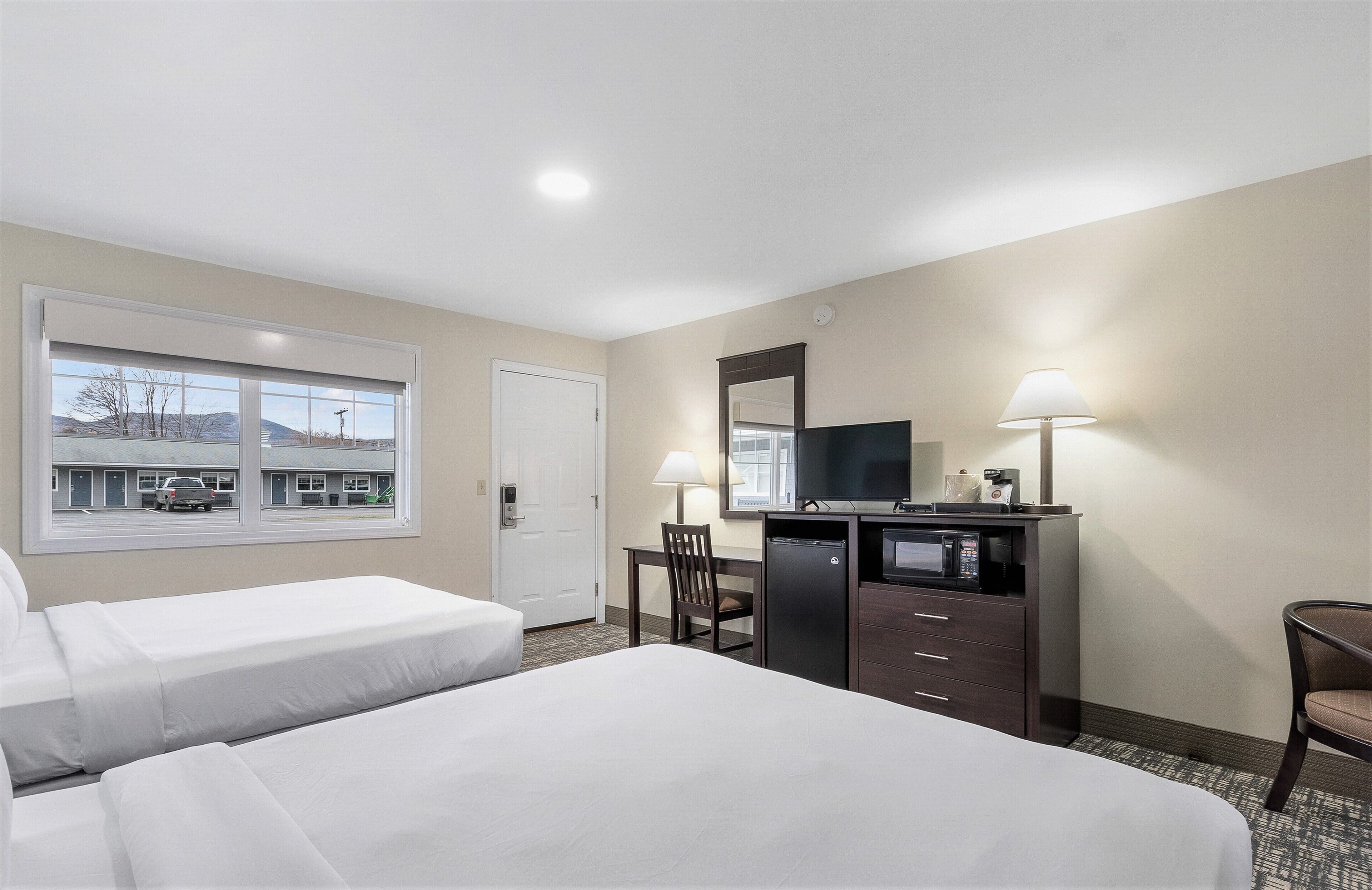 A hotel room with two beds, a desk with a TV, a lamp, and a view of a building outside.
