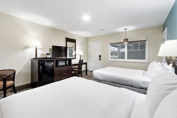 A hotel room with two beds, a desk with a chair, a television, and a window with a view of a parking garage.