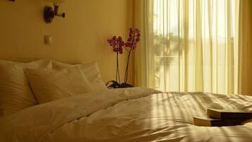 A bed with white bedding, a vase with purple flowers, and two books on the bed.
