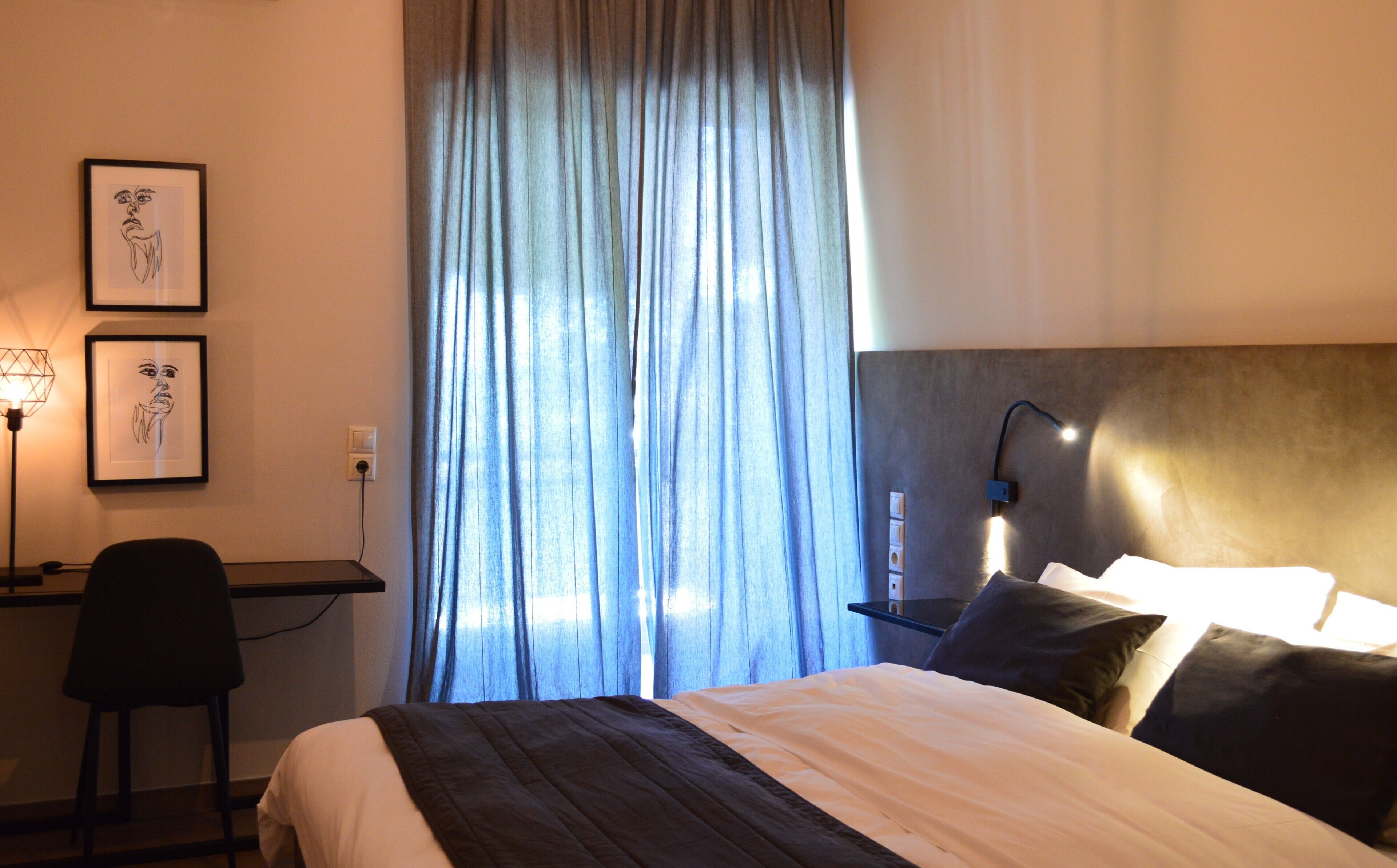 Una habitación de hotel con cama, escritorio, silla, lámpara y ventana con cortinas.