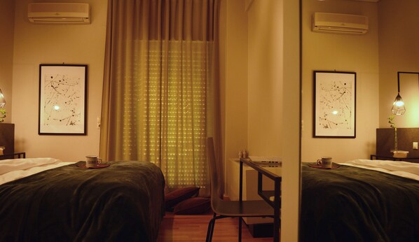 A hotel room with two beds, a desk, a chair, and two air conditioning units.