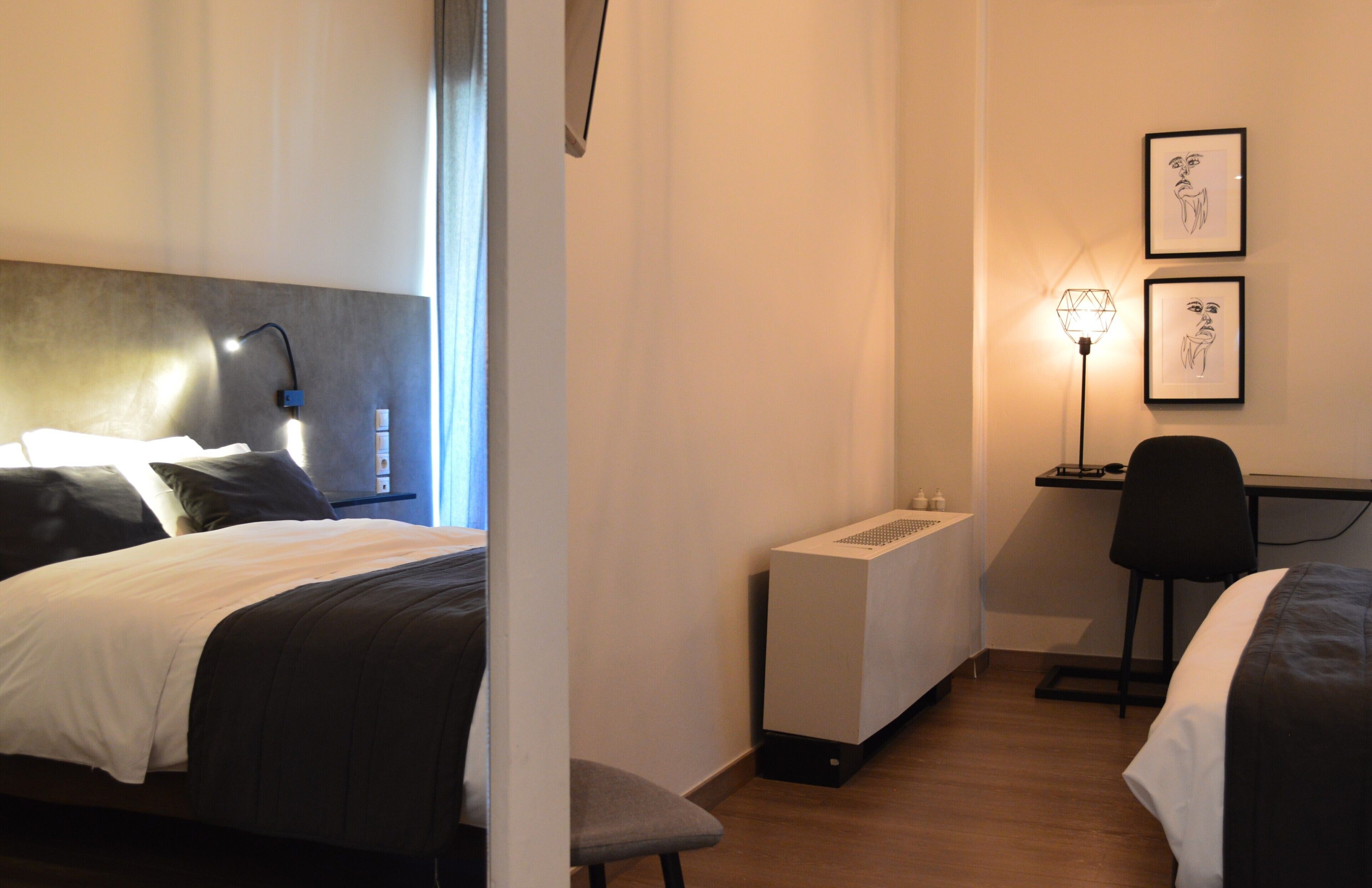 A hotel room with two beds, a desk, a chair, a standing heater, and two framed pictures on the wall.