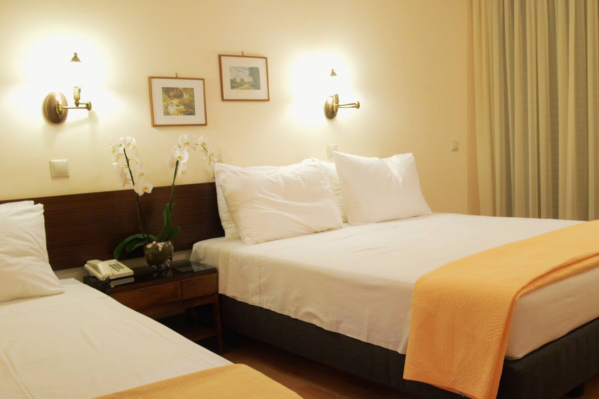 A hotel room with a bed, bedside table, lamp, framed pictures, and a window with curtains.