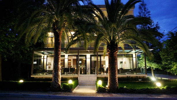 Un hotel moderno con fachada de vidrio, palmeras y una entrada bien iluminada.