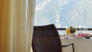 Un comedor con vista a la montaña, una silla y alimentos para el desayuno sobre la mesa.